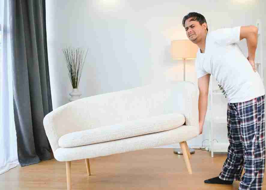 a man suffering from back ache while carrying a couch